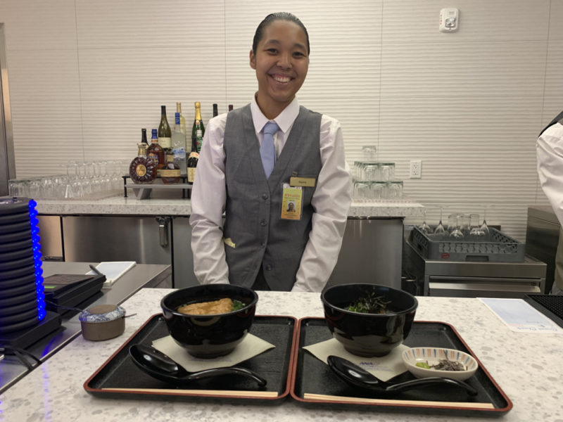 a woman standing behind a counter with bowls of food