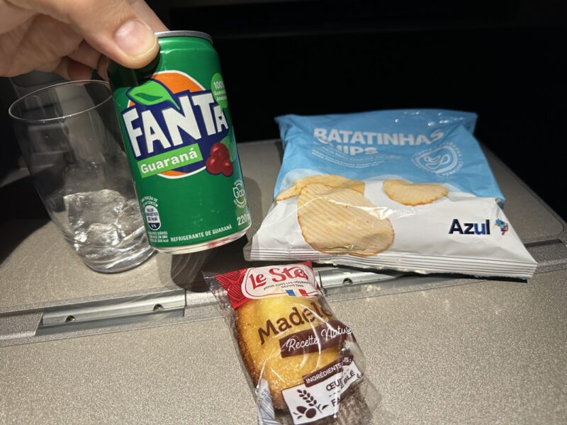 a hand holding a can of soda next to a bag of chips