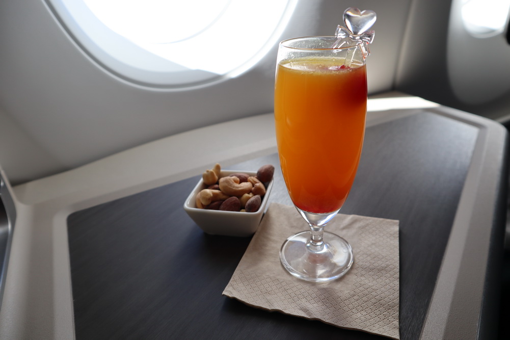 a glass of orange liquid next to a bowl of nuts