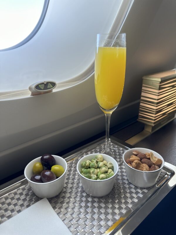 a glass of orange juice next to bowls of nuts and fruits