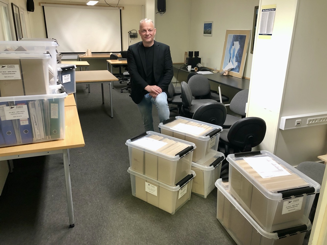 a man sitting in an office with many plastic bins