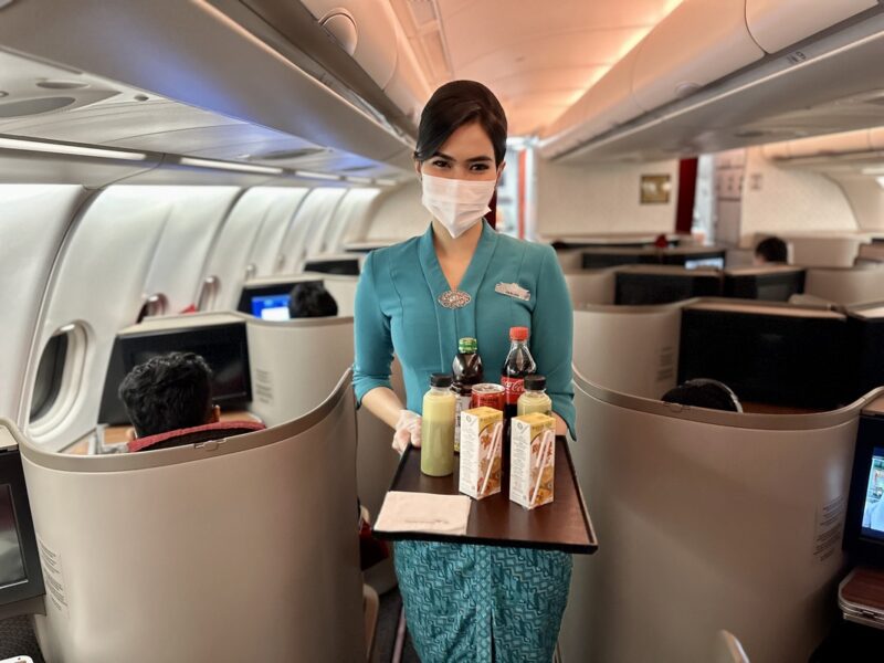 a woman wearing a mask and gloves holding a tray with drinks and beverages