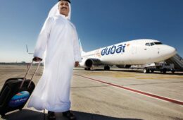 a man in a white robe with a suitcase standing in front of an airplane