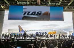 a man on a stage with a crowd watching a large screen with airplanes