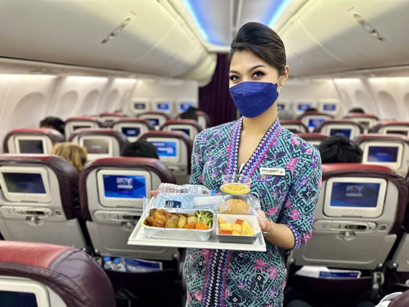 a woman wearing a face mask holding a tray of food in an airplane