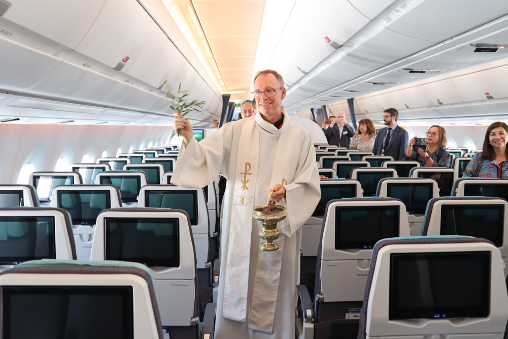 a man in a white robe holding a cup and a plant in a row of seats