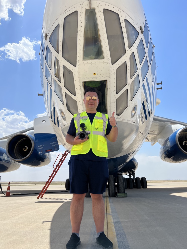 a man in a yellow vest holding a camera in front of a plane